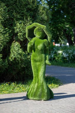 Yeşil elbiseli bir kadın bir ağacın önünde duruyor. O bir şemsiye tutuyor.