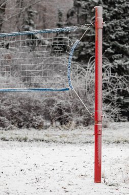 Bir voleybol ağı karla kaplıdır. Ağ kırmızı ve mavi. Kar beyaz ve zemin karla kaplı.