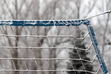 Karla kaplı bir futbol ağı. Ağ mavi ve beyazdır. Kar ağı ve zemini kaplıyor.