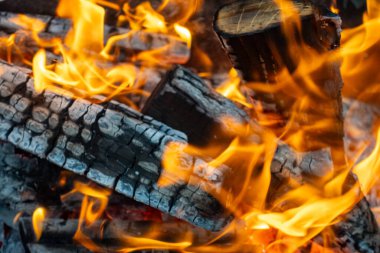 A pile of wood with a lot of flames coming from it. The fire is very hot and the wood is charred, giving the scene a sense of danger and intensity. The flames are reaching up high