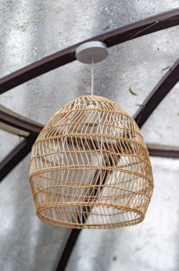 A lamp hanging from a ceiling with a wicker shade. The lamp is hanging from a metal rod