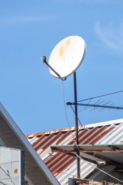 Çatıda bir uydu anteni var. Tabak beyaz ve paslı. Gökyüzü mavi ve berrak