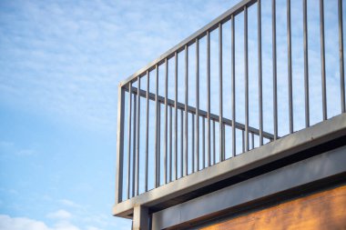 Arka planda açık mavi gökyüzü olan bir balkon korkuluğu. Korkuluklar metalden yapılmıştır ve çok uzundur.