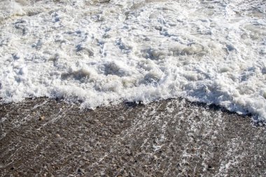 Bir dalga kayalık bir sahile çarpıyor. Su beyaz ve köpüklü ve kayalar sahnenin her tarafına saçılmış. Sahne güç ve enerjiden oluşur, dalgalar kıyıya çarpar.