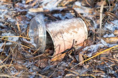 Yerde kapağı eksik plastik bir bardak var. Bardak kirli ve içinde bir delik var. İhmal ve israf kavramı, çünkü kupa çöpe atıldı ve toprağa bırakıldı.