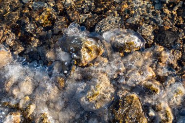 Kayalık bir kıyı şeridi olan bir su kütlesi. Su donmuş ve kayalar sahnenin her tarafına saçılmış. Sahne sakin ve huzurlu, donmuş su ve kayalar sükunet yaratıyor.