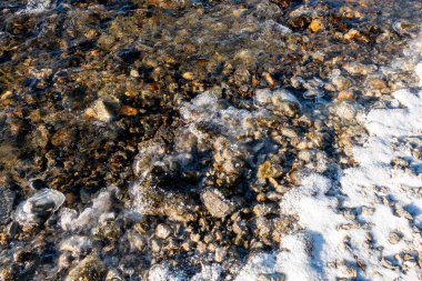 Önünde bir su kütlesi olan kayalık bir kıyı şeridi. Su donmuş ve kayalar etrafa saçılmış.