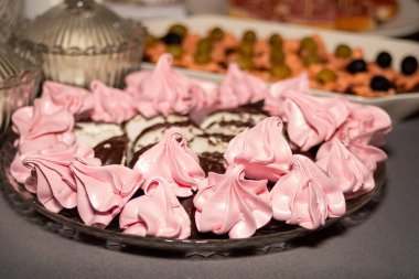 A plate of pink frosted pastries with chocolate drizzle. The plate is on a table and surrounded by other food items