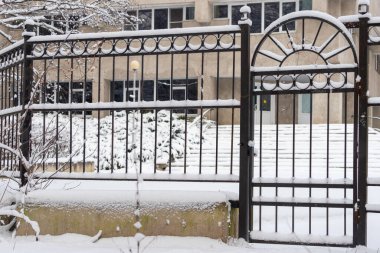 Bir kapı karla kaplıdır ve bir binanın önünde yer alır. Kapı açık ve üzerinde bir tasarım var.