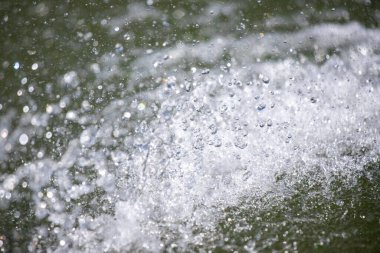 Gökten bir sürü su damlası düşen büyük bir su kütlesi. Su damlacıkları suyun her tarafına dağılmış, hareket ve enerji hissi yaratıyorlar. Manzara canlı ve dinamiktir.