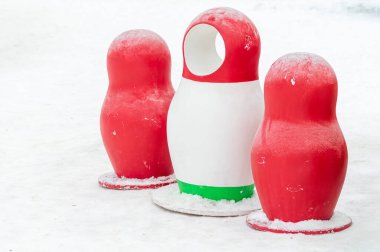 Üç kızıl Rus bebeği karla kaplı bir zeminde oturuyorlar. Bebeklerden birinin kafası kayıp.