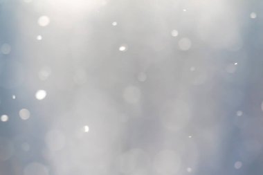 Gri arkaplanı olan kar tanelerinin bulanık bir görüntüsü. Kar taneleri görüntünün her tarafına dağılmış, hareket ve kaos hissi yaratıyor. Gri arkaplan resmin genel moduna ekler