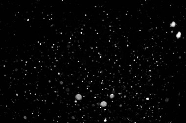 Gökyüzünden düşen kar tanelerinin siyah beyaz bir fotoğrafı. Kar taneleri yavaşça yere düşerken sakinlik ve sükunet kavramı. Fotoğraftaki renk eksikliği saflığı vurguluyor.