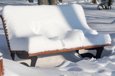 Parkta karla kaplı bir bank oturuyor. Kar bankın üzerine yığılmış, dev bir kardan adam gibi görünüyor. Sahne huzurlu ve sakin, kar bankı kaplıyor.