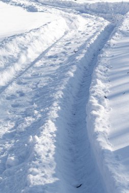 Sağda kar izi olan karla kaplı bir patika. Kar derin ve yol dar.