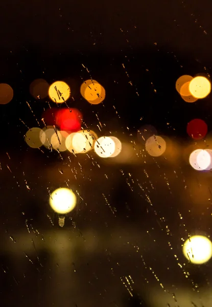 Abstraktes nächtliches Stadtlicht und Bokeh durch die Windschutzscheibe des Autos, die mit Regen bedeckt ist — Stockfoto