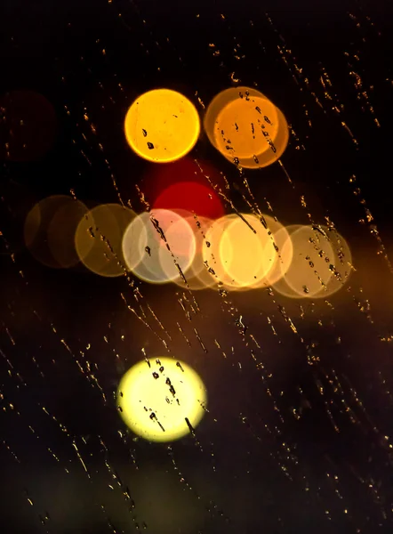 Abstraktes nächtliches Stadtlicht und Bokeh durch die Windschutzscheibe des Autos, die mit Regen bedeckt ist — Stockfoto