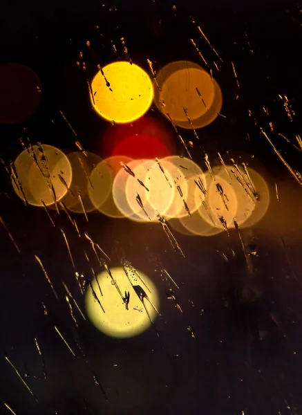 Abstraktes nächtliches Stadtlicht und Bokeh durch die Windschutzscheibe des Autos, die mit Regen bedeckt ist — Stockfoto