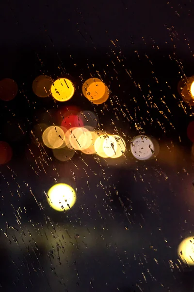 Abstraktes nächtliches Stadtlicht und Bokeh durch die Windschutzscheibe des Autos, die mit Regen bedeckt ist — Stockfoto