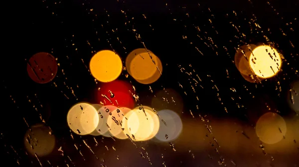 Abstraktes nächtliches Stadtlicht und Bokeh durch die Windschutzscheibe des Autos, die mit Regen bedeckt ist — Stockfoto