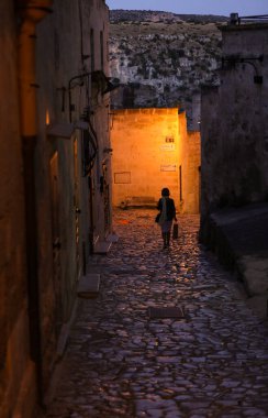 Matera, İtalya - 14 Eylül 2019: Matera şehrinin tarihi bir bölgesi olan Sassi di Matera 'daki Cobblestone caddesinde bir yürüyüş yapan kadın. Basilicata. İtalya