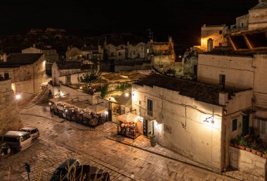 Matera, İtalya - 19 Eylül 2019: Matera, İtalya 'nın akşam manzarası, Sassi di Matera şehrinin tarihi bir bölgesi olan Sassi di Matera' daki kaldırım kafelerinin avlularını aydınlatan renkli ışıklarla. Basilicata. İtalya