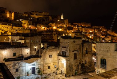 Matera 'daki antik Sassi bölgesinde geceleri, antik mağara evleri ile tanınan şaşırtıcı aydınlık binalar. Basilicata. İtalya
