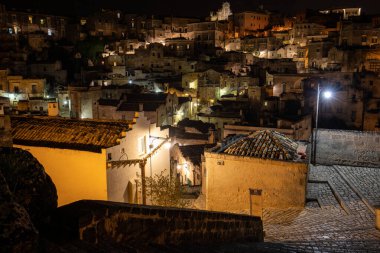 Matera 'daki antik Sassi bölgesinde geceleri, antik mağara evleri ile tanınan şaşırtıcı aydınlık binalar. Basilicata. İtalya