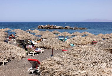 Kamari, Santorini, Yunanistan - 27 Haziran 2021: Santorini 'deki siyah volkanik Kamari plajında güneş pansiyonları. Cyclades, Yunanistan