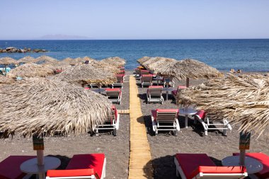 Kamari, Santorini, Yunanistan - 27 Haziran 2021: Santorini 'deki siyah volkanik Kamari plajında güneş pansiyonları. Cyclades, Yunanistan