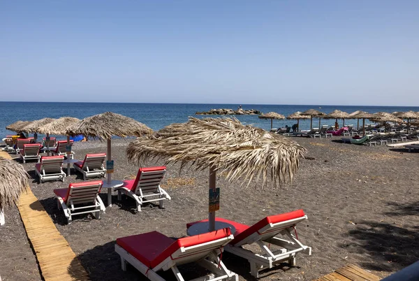 Kamari, Santorini, Yunanistan - 27 Haziran 2021: Santorini 'deki siyah volkanik Kamari plajında güneş pansiyonları. Cyclades, Yunanistan