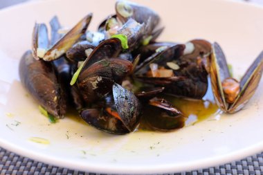 Beyaz bir tabakta beyaz şarap soslu enfes taze midyeler.