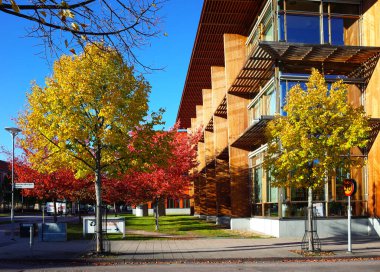 Vasteras, İsveç - 3 Ekim 2018: Lise kütüphanesinin modern binası yakınlarında kırmızı ve sarı sonbahar renklerinde ağaçlar