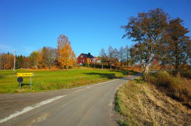 Ivarbyn, İsveç - 15 Ekim 2018: İsveç 'te sonbahar, yolu olan kır manzarası, Skraddarbo işareti, büyük ağaç, yeşil alan ve geleneksel kırmızı ahşap İsveç evi