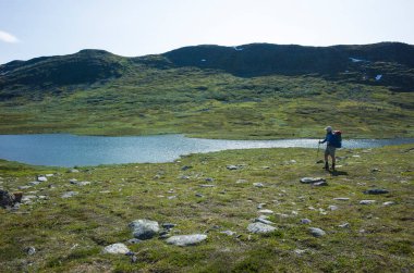 İsveç Laponya 'sında yürüyüş. İnsan gezgin İsveç 'teki dağ gölü manzarasıyla tek başına yürüyor. Kuzey Kutbu, İskandinavya 'nın doğası sıcak yaz güneşli ve mavi gökyüzü