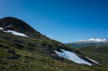 İsveç Laponya 'daki Stuor Allagas Tepesi' nin yamacında kar, İskandinavya 'nın kutup doğası sıcak yaz güneşli bir günde mavi gökyüzü...