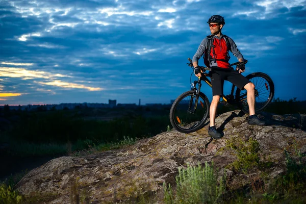 Ciclista descansando con bicicleta de montaña en la roca al atardecer — Foto de Stock