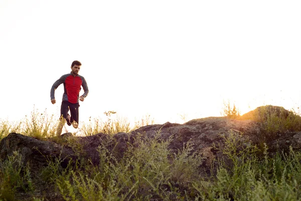 Junger Sportler, der bei Sonnenuntergang auf dem steinigen Bergpfad läuft. Aktiver Lebensstil — Stockfoto