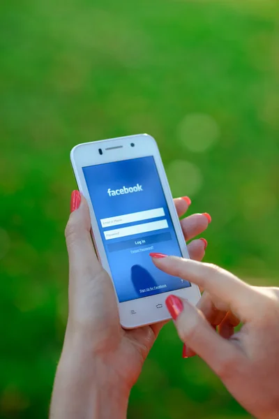 DNIPROPETROVSK, UCRANIA - 19 DE SEPTIEMBRE DE 2014: Mujer joven usando la aplicación de red social de Facebook en su teléfono inteligente . —  Fotos de Stock