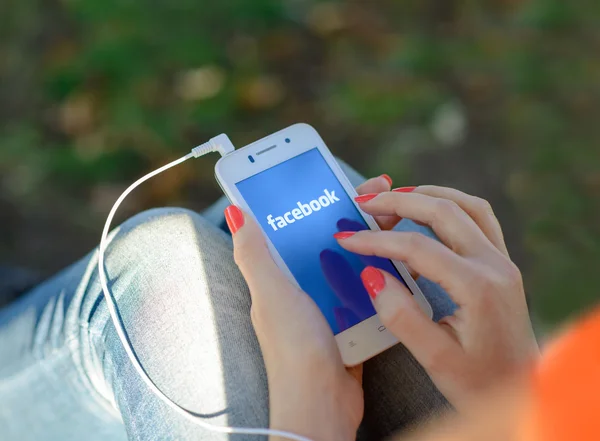 DNIPROPETROVSK, UCRANIA - 18 DE SEPTIEMBRE DE 2014: Mujer joven usando la aplicación de red social de Facebook en su teléfono inteligente . —  Fotos de Stock