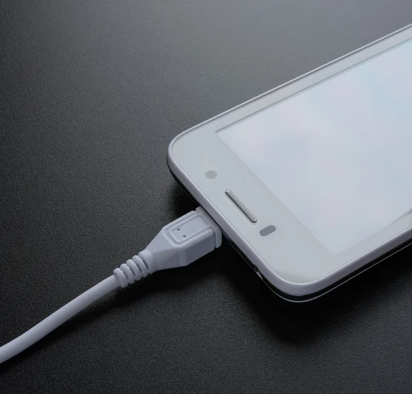 Белый смартфон зарядки с кабелем USB на черном столе — стоковое фото