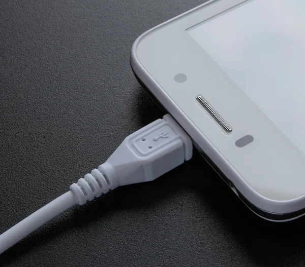 Weißes Smartphone aufladen mit USB-Kabel auf schwarzem Tisch — Stockfoto