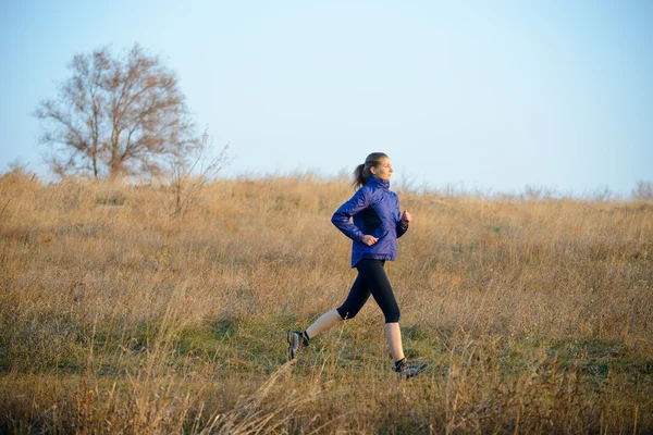Jovem mulher esportiva correndo na trilha no campo de outono — Fotografia de Stock