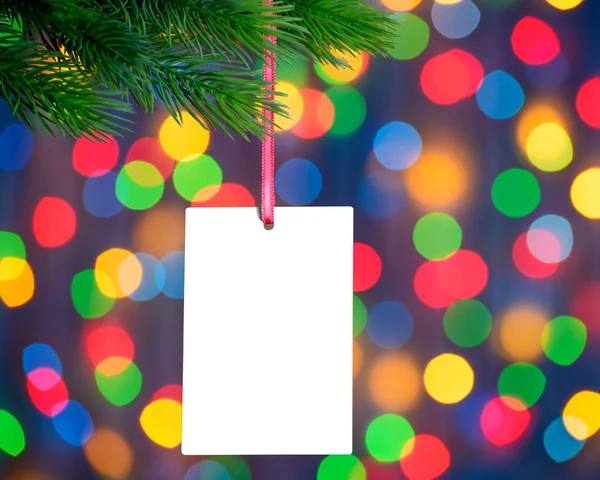 Weihnachtsgrußkarte auf dem Tannenzweig auf dem Hintergrund der Weihnachtsbeleuchtung — Stockfoto