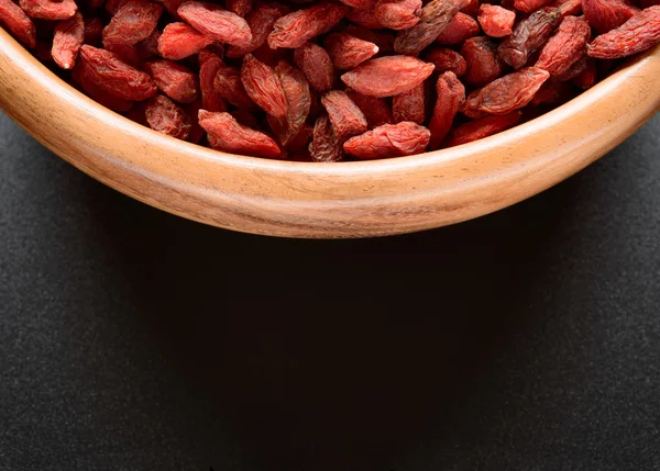 Tigela de madeira cheia de bagas secas Goji na mesa preta — Fotografia de Stock