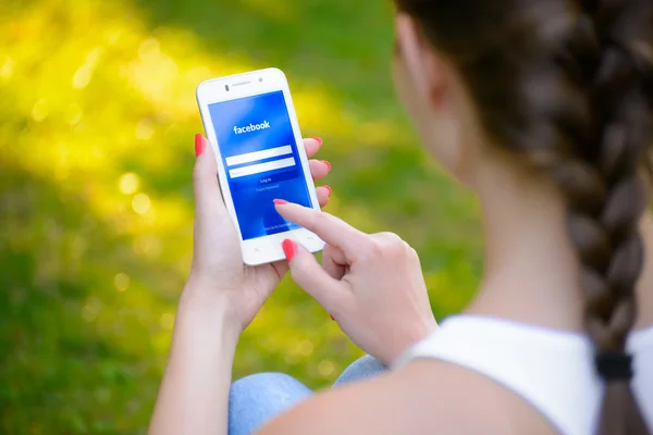 Zaporizhzhya, Ukraine - 20. September 2014: junge Frau nutzt Facebook-Anwendung für das soziale Netzwerk auf ihrem Smartphone. — Stockfoto