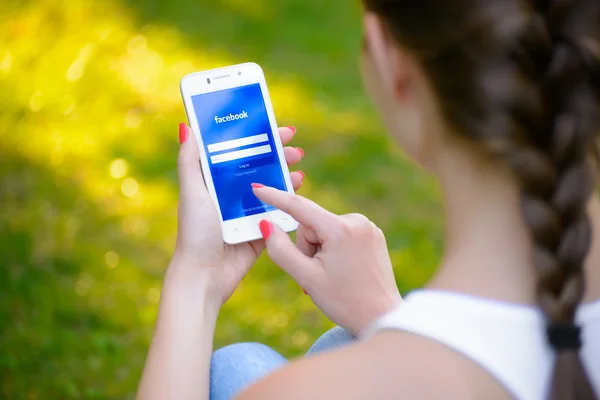 ZAPORIZHZHYA, UCRANIA - 20 DE SEPTIEMBRE DE 2014: Mujer joven usando la aplicación de red social de Facebook en su teléfono inteligente . — Foto de Stock