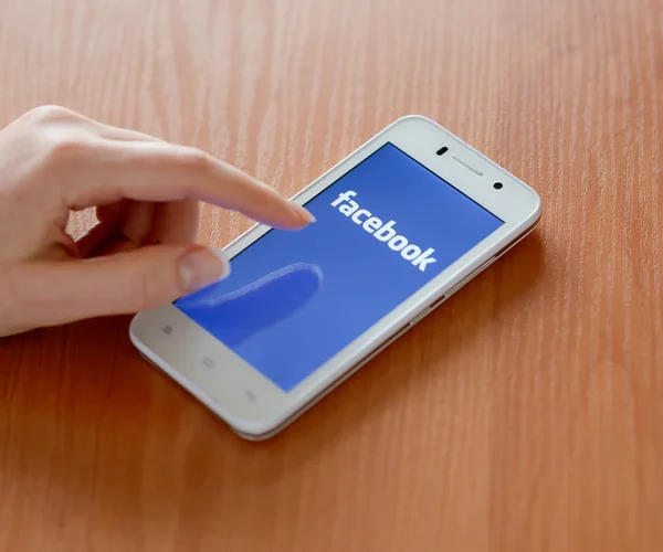 ЗАПОРИЖЬЯ, УКРАИНА - 23 ЯНВАРЯ 2015: Молодая женщина использует приложение социальной сети Facebook на своем смартфоне . — стоковое фото
