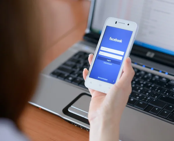 ZAPORIZHZHYA, UCRANIA - 23 DE ENERO DE 2015: Mujer joven usando la aplicación de red social de Facebook en su teléfono inteligente . —  Fotos de Stock