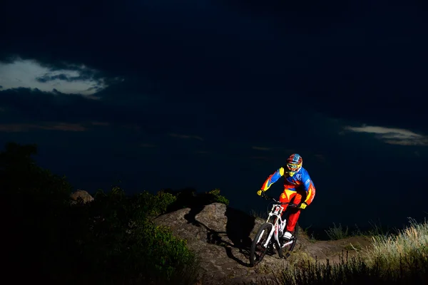 Fully Equipped Professional Downhill Cyclist Riding the Bike on the Night Rocky Trail Ліцензійні Стокові Фото
